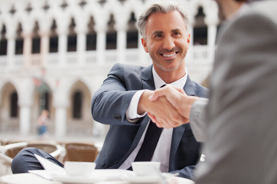 Smiling businessmen shaking hands at sidewalk cafe