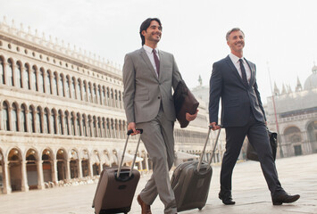 Smiling businessmen walking suitcases through St. Mark's Square in Venice