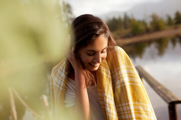 Smiling woman wrapped in blanket at lakeside