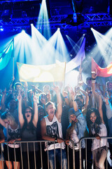 Crowd cheering with arms raised behind railing at concert