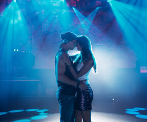 Couple dancing kissing under spotlights empty dance floor of nightclub