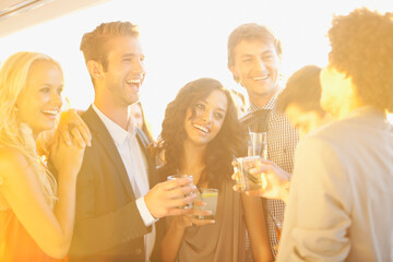 Smiling friends drinking cocktails on sunny balcony