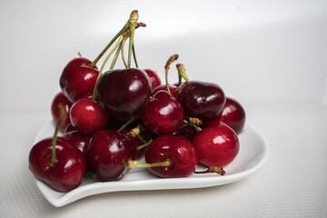 Sweet red cherry in a white porcelain plate on a white background. Closeup.