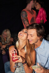 Laughing couple hugging and drinking cocktails in nightclub