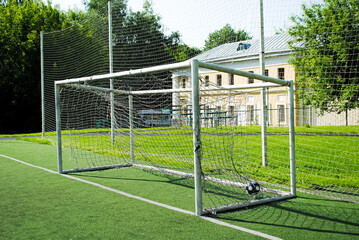 A ball in a soccer goal on an amateur soccer field on a sunny summer day. Gates with a torn and dirty net. Sports group games on a professional and amateur level. Summer outdoor sports.