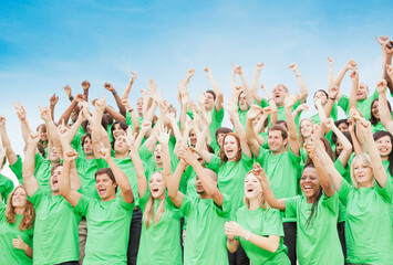 Crowd in green t-shirts cheering with arms raised