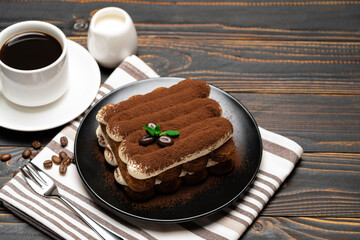 Classic tiramisu dessert on ceramic plate, milk or cream and cup of coffee on wooden background