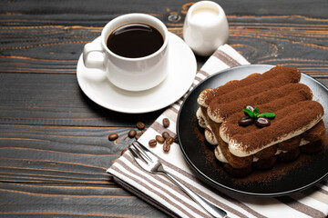 Classic tiramisu dessert on ceramic plate, milk or cream and cup of coffee on wooden background