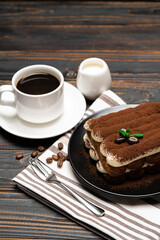 Classic tiramisu dessert on ceramic plate, milk or cream and cup of coffee on wooden background