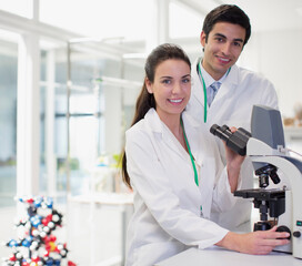 Portrait of smiling scientists using microscope in laboratory