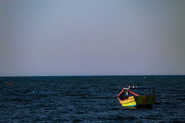Obraz premium fishing boat at sea. Blue, yellow and red fishing boat at sea with blue sky in the background.
