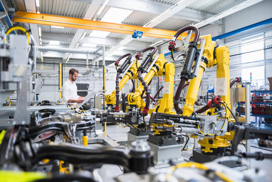 Young engineer reading paper while standing by robotic arms in automated industry