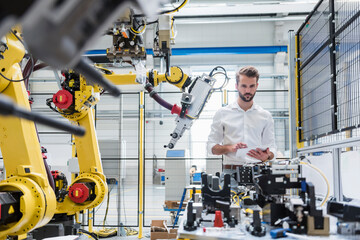 Young engineer holding digital tablet while looking at machinery in factory