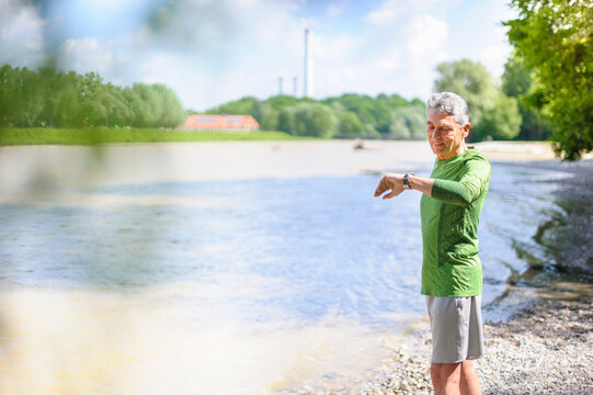 Active elderly man checking time while standing at riverbank on sunny day