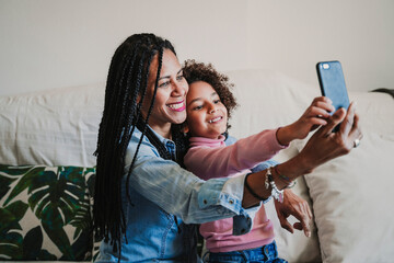 Happy mother and her little daughter taking selfie with smartphone at home