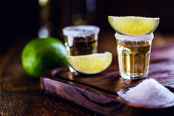 small glass of tequila, fiery drink from mexico. Lemon, coarse salt on wooden background.