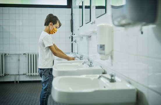 Boy wearing mask on school toilet washing his hands