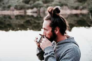 Man drinking from mug at lakeside
