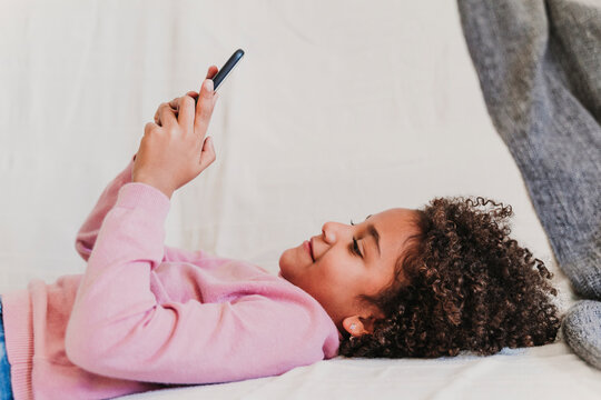 Portrait of happy little girl lying on the couch looking at smartphone