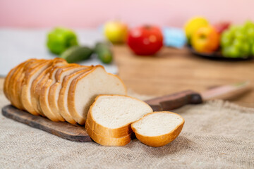 chopped long loaf on a cutting board next to a tomato, cucumber and pepper