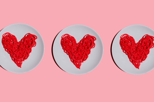 Studio shot of three plates with red-colored heart-shaped spaghetti against pink background