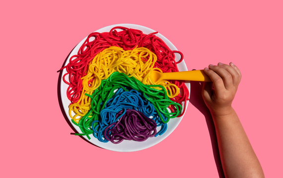 Hand of baby girl eating rainbow-colored spaghetti