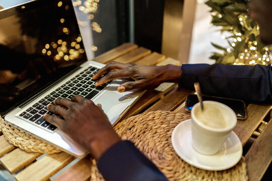Crop view of young businessman working on laptop in a coffee shop - Powered by Adobe