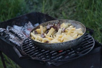 jacket potatoes, squash and sausages are cooked in a large frying pan on an open fire