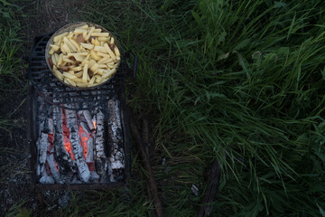 Sliced raw potatoes in a pan over charcoal. Outdoor barbecue. Preparing food