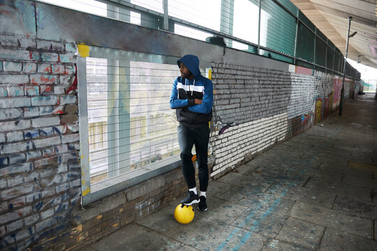 Yung man with football leaning on wall and looking through grid