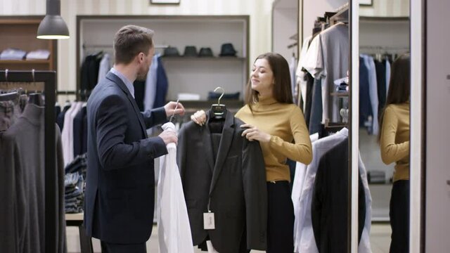 A side view panoramic shot of a young clothing shop consultant helping a male buyer create a new clothing style
