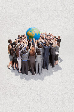 Crowd Of Business People In Huddle Lifting Globe Overhead