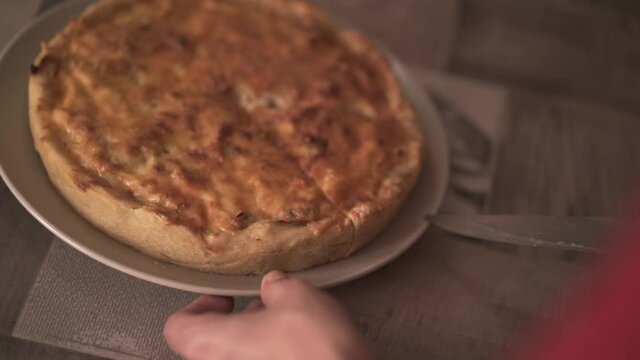 Baked pie ready for dinner on a glass plate. Action. Close up of hands cutting with a knife prepared homemade tasty pie with crispy crust on kitchen table background.