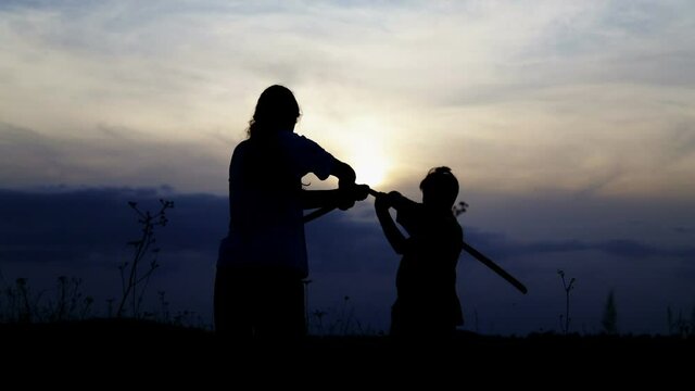 Teenage boys fencing with samurai training swords. Silhouette of exercising children in a field with swords.