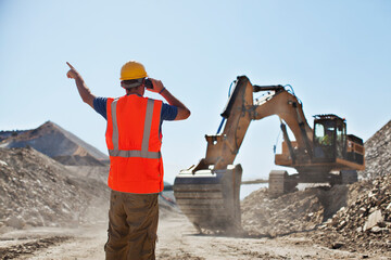 Worker directing digger in quarry