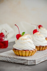 Tartlets with cherry filling and Italian meringue with a cocktail cherry on top on a board on a concrete background. Vertical orientation. Copy space. Food background.