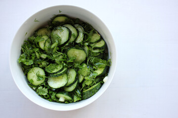 Summer fresh cucumber, dill, parsley, green onion salad in a white ceramic bowl on white wooden background. Top view 
