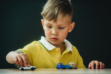 a boy in a bright T-shirt plays little cars at the table