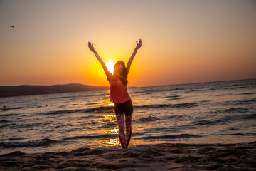 Obraz premium Happy woman standing on the sand beach with hands up, open arms at beautiful sunrise on seaside