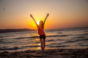 Happy woman standing on the sand beach with hands up, open arms at beautiful sunrise on seaside