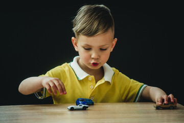a boy in a bright T-shirt plays little cars at the table