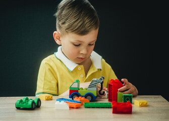 a boy in a bright T-shirt plays in a multi-colored designer at the table