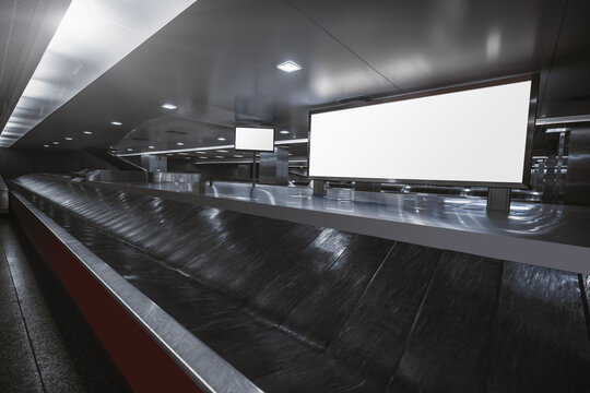 Wide-angle View Of A Baggage Claim Area In A Hall Of A Modern Airport Arrival Zone With Luggage Conveyor Belt And A Mock-up Of White Empty Advertising Or Information Billboard And Tv Plasma Screen