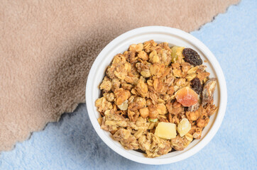 Muesli in a round cup with a dessert spoon on a blue and beige background. Added to milk or yogurt for breakfast. Selective focus.