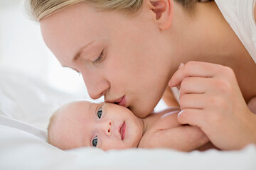 Obraz na płótnie Canvas Mother kissing newborn baby on bed