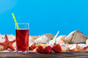 Ripe red Strawberry. Orange juice in a glass on the shore of the sea beach on a sunny day. Sunny rest during the holidays.
