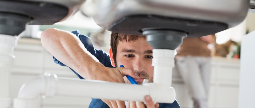 Plumber Working On Pipes Under Sink