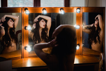 Sensual nude pretty young female sitting in front of mirror holding her head fine art nude