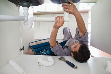 Plumber working on pipes under kitchen sink