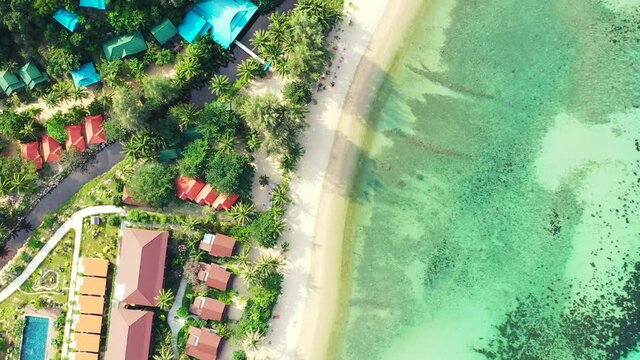 Zoom-in, bird's eye view of a resort village with a beautiful pristine white sea shore and turquoise waters, top view.